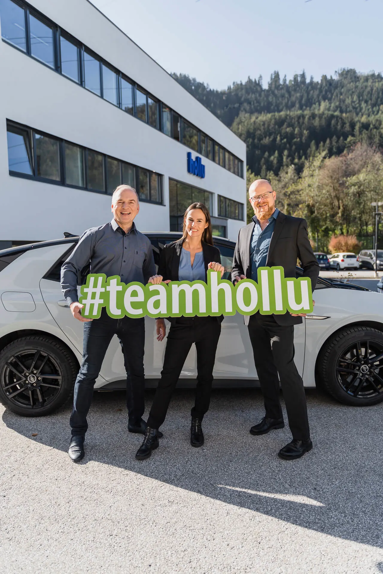 3 persomen mit einem schild #teamhollu vor einem weißen auto