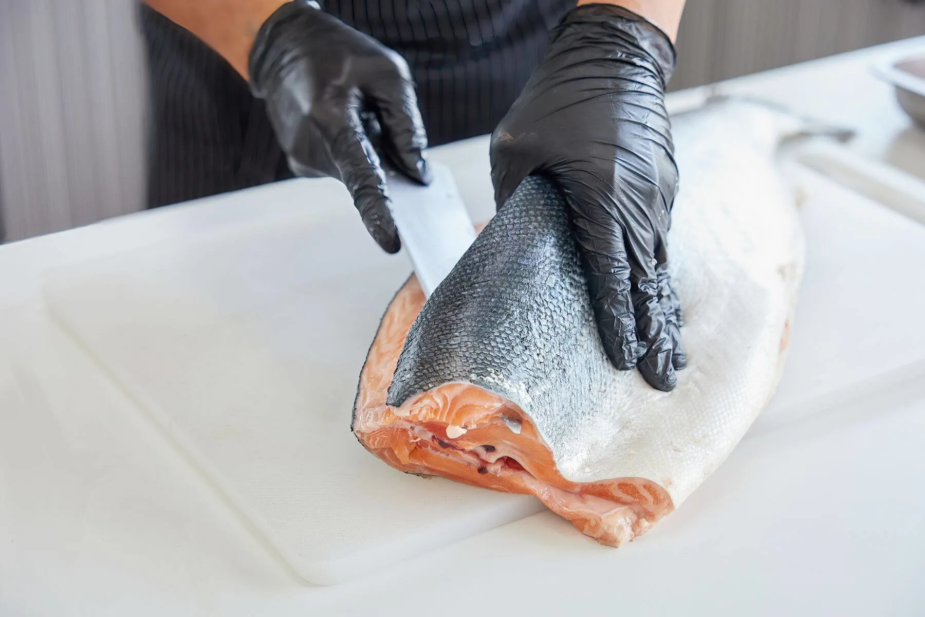 ein fisch wird von händen mit schwarzen handschuhen filetiert