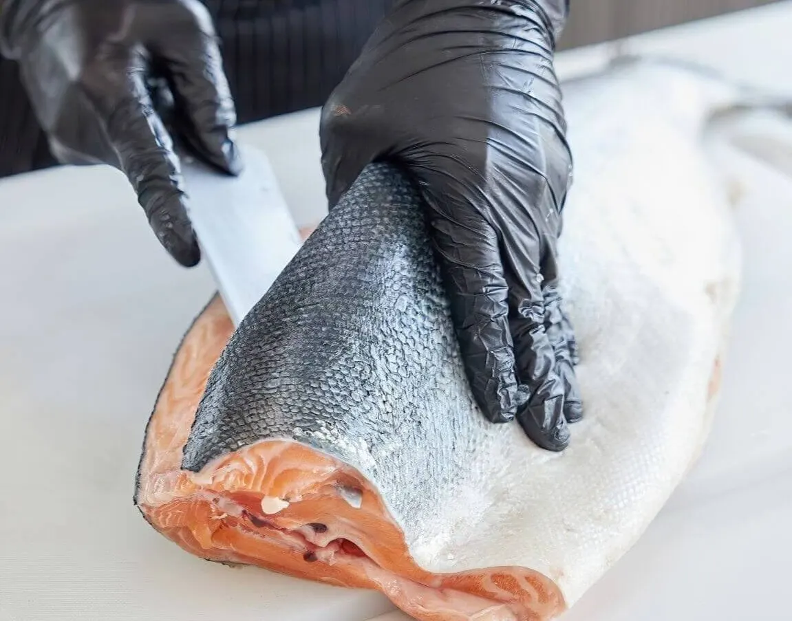 ein fisch wird von händen mit schwarzen handschuhen filetiert