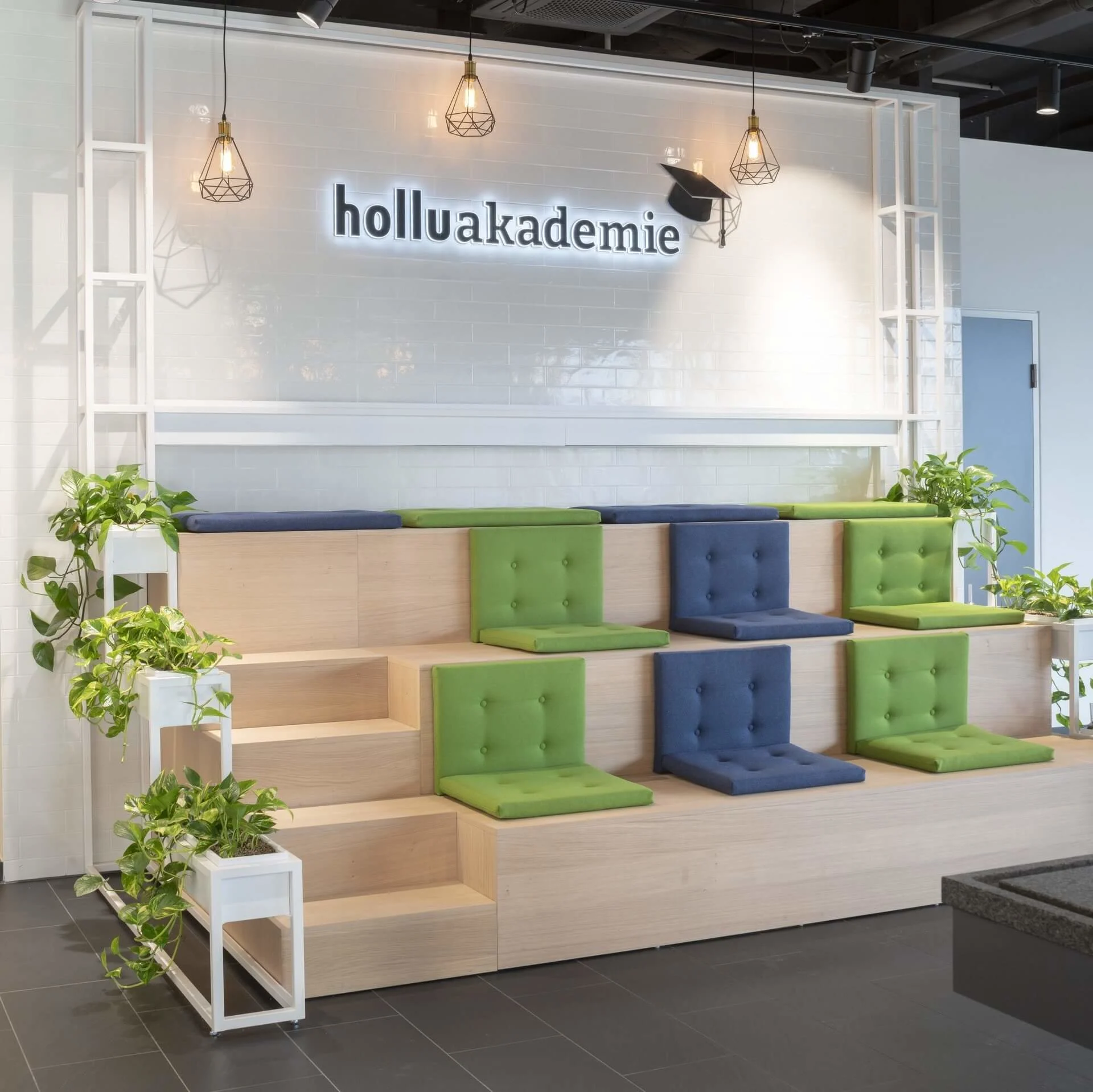 eine sitztreppe it blauen und grünen pölstern und dem schriftzug "holluakademie"
