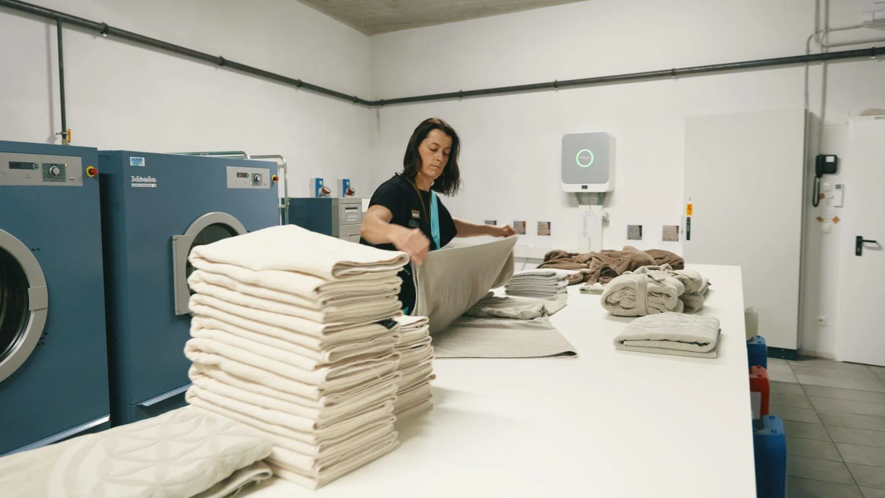 Mitarbeiterin faltet saubere Handtücher in einer professionellen Wäscherei neben industriellen Waschmaschinen.